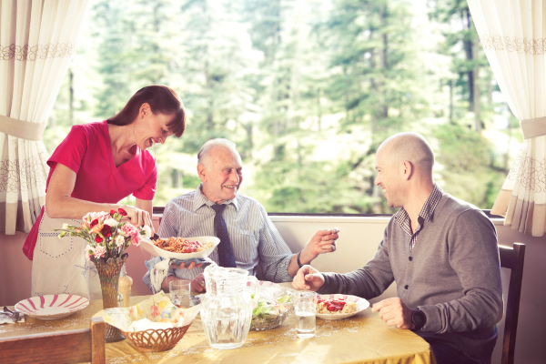 A smiling Nurse Next Door Caregiver serving food to a father and son